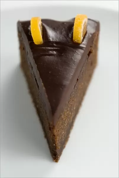 Slice of rich dense dark chocolate cake with shiny choc topping and candied orange