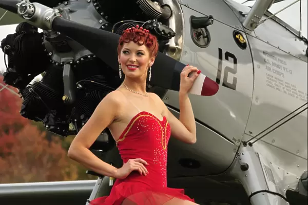 Redhead pin-up girl in 1940s style dancer attire holding on to a vintage aircraft
