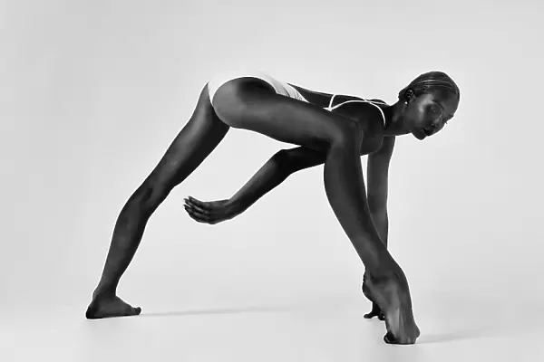young ballerina in a bodysuit stands in a lunge leaning forward with one foot on the toe