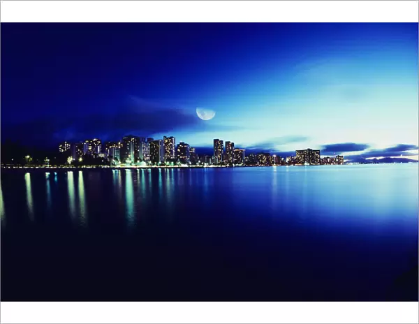 Hawaii, Oahu, Honolulu, Waikiki skyline at night, moon overhead, view from ocean