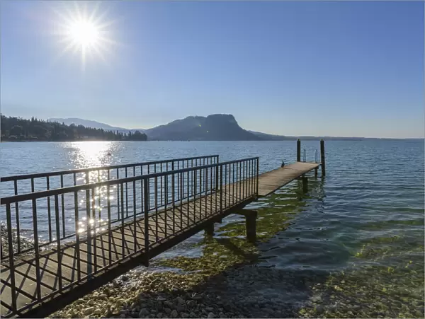 Sun shining on Lake Garda (Lago di Gardo) with wooden jetty in the summer at Garda in Veneto, Italy