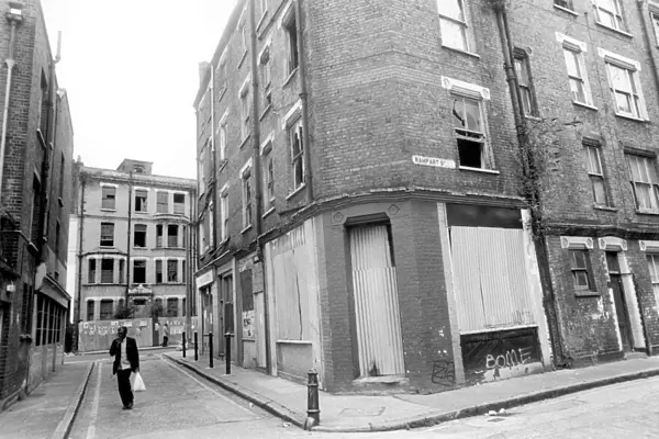 A man carrying his shopping bag as he walks past delapidated buildings with broken