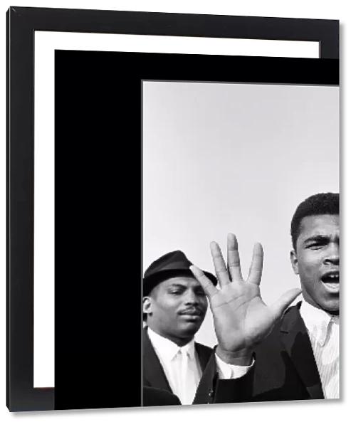 Cassius Clay aka (Muhammad Ali) on arrival at London Airport He holds up five