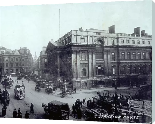 Angle shot of the Mansion House in London, official residence of the mayor of the city. In the foreground, wide street in front of and at the side of the building, with many people and horse-drawn gigs