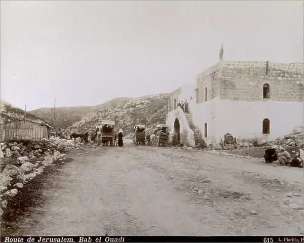 Middle eastern travellers with carts and horses on the road for Jerusalem. A poor house stands along the road where there are some people sitting