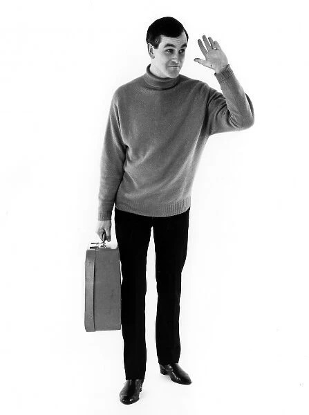 HEs OFF. A man waves with one hand and holds his suitcase with the other. Date: late 1960s