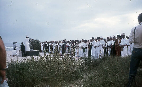 Men stand praying by the beach in Oman