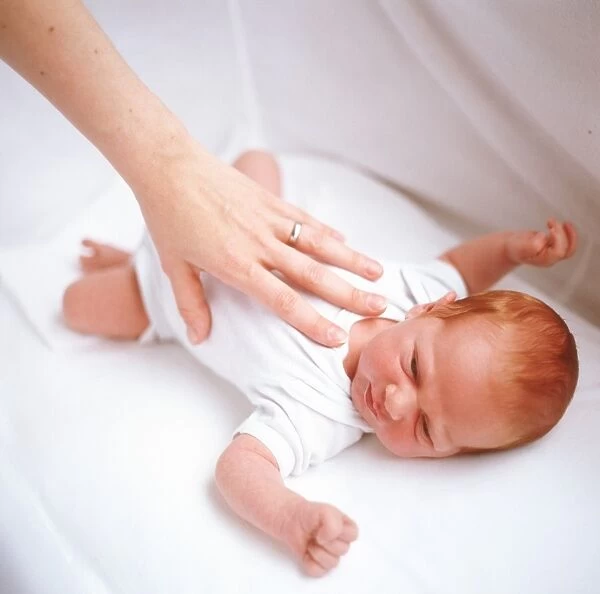 Baby boy. MODEL RELEASED. Baby boy being comforted by his mothers hand