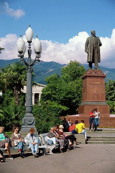 People sitting on benches near a statue of Lenin in Yalta