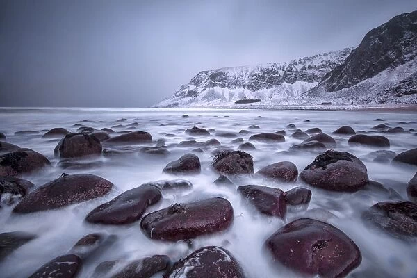 Rocks on the beach modeled by the wind surround the icy sea, Unstad, Lofoten Islands
