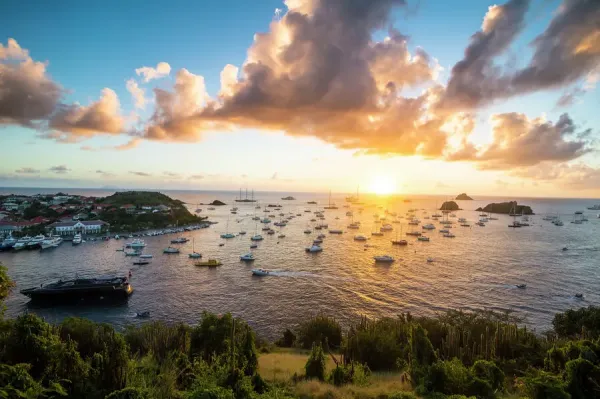 Sunset over Gustavia Harbor, golden sky reflecting on yachts and town lights