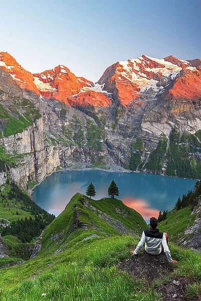 View of a hiker resting in front of the Oeschinensee lake surrounded by snowy peak at sunset, Oeschinensee, Kandersteg, Bern Canton, Switzerland, Europe