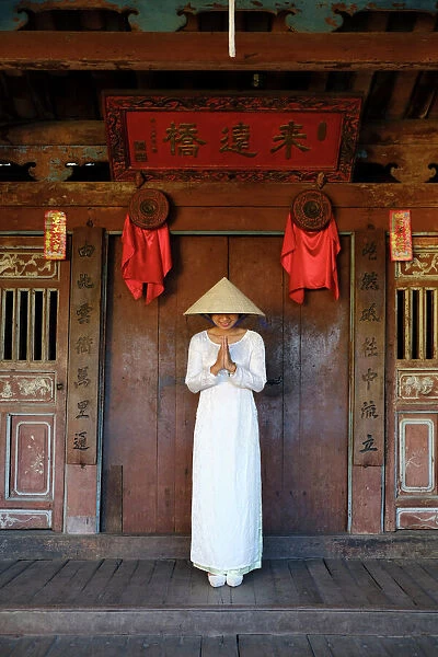 A young woman in a Non La conical hat and a traditional Ao Dai dress in the historical centre