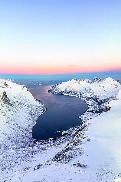 Aerial panoramic of snowcapped mountains and coastal village of Bergsfjord at winter dawn, Senja, Troms county, Norway