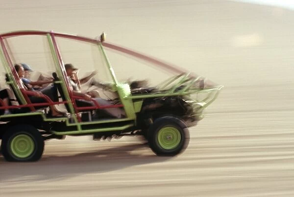 A dune buggy speeds tourists acoss through the sand