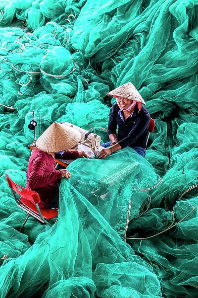 Vietnam, Cam Ranh, two men repair green fishing nets using