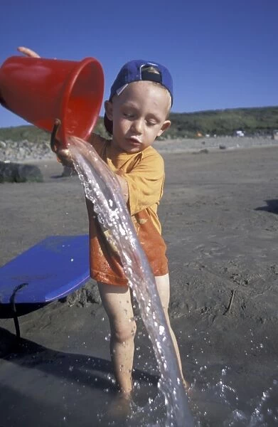 Boy pouring water from a bucket, Whitesands Beach, St Davids, Pembrokeshire, Wales, UK, Europe