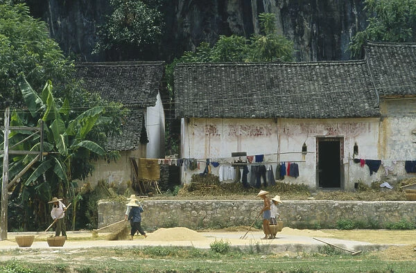 10073205. CHINA Guangxi Province People drying grain outside a farmhouse