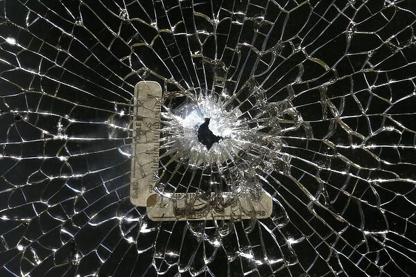 A bullet hole is seen on a cracked window at a gym next to the scene where three police