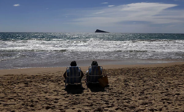 A couple relaxes as they sunbath on a beach during a sunny day in Benidorm