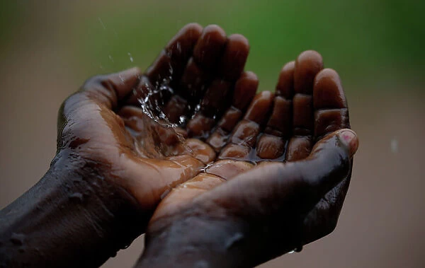 A Malawian child catches raindrops during a brief downpour in Ngozi village near the