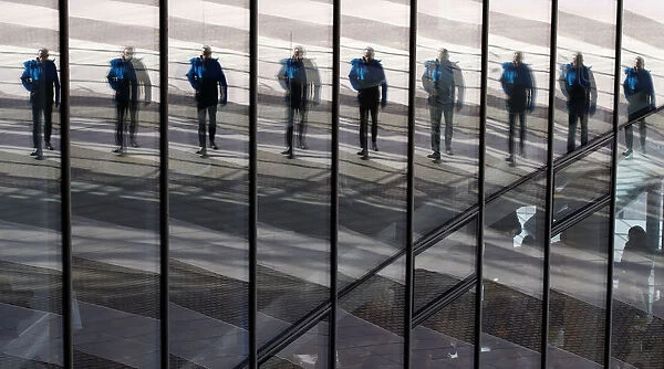 A man is reflected in the glass facade of the Post Tower, the headquarters of German postal