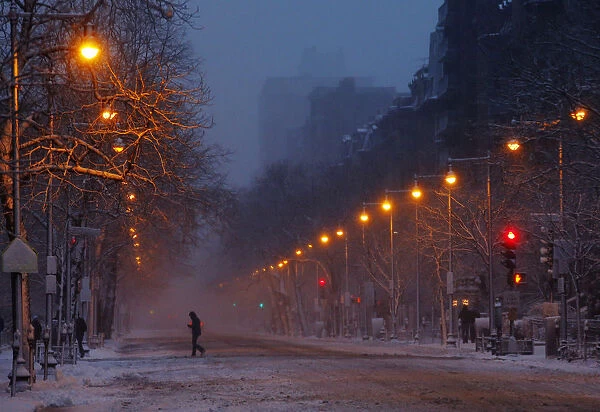 A pedestrian crosses Beacon Street as snow begins to accumulate in Boston