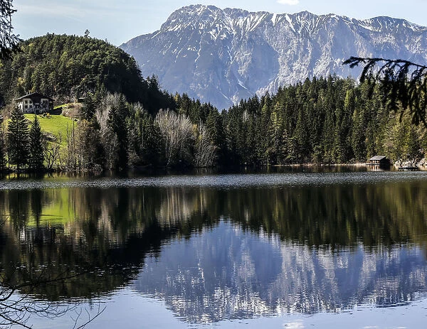 Snow covered mountains are reflected in Piburger lake on a sunny spring day in the