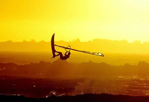 WINDSURFERS GETS AIRBOURNE AS THE SUN SETS ON CAPE TOWNs BLaUBERG BEACH