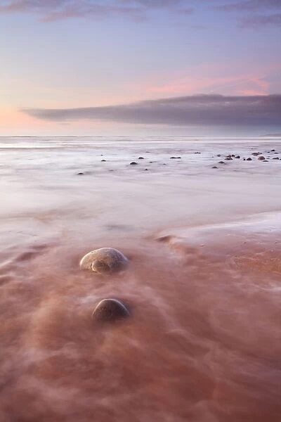 View of pebbles on beach with incoming tide at sunset, Westward Ho!, North Devon, England, january