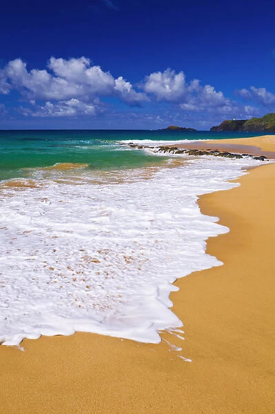 Surf, sand and blue green waters at Secret Beach (Kauapea Beach), Kilauea Lighthouse visible