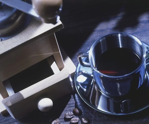 Abstract overhead view of a metal cup containing coffee on a metal saucer with a coffee grinder also visible