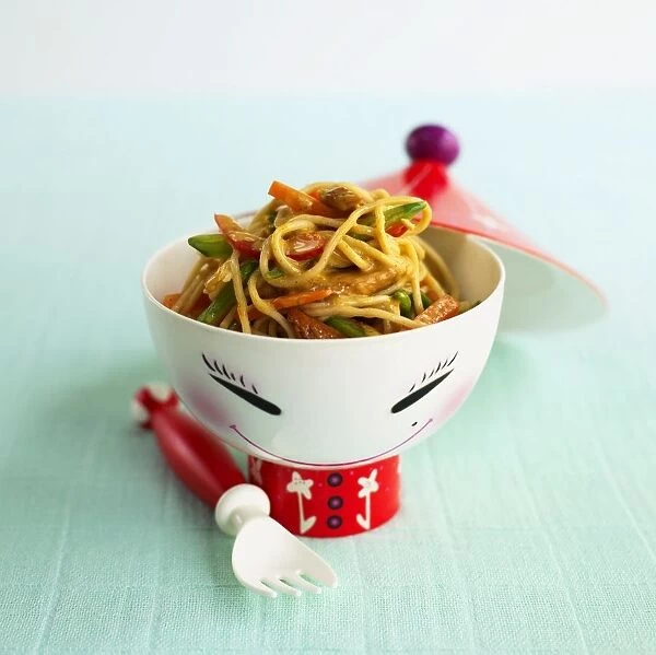 Chicken and vegetable noodles in bowl with face painted on, lid and fork nearby