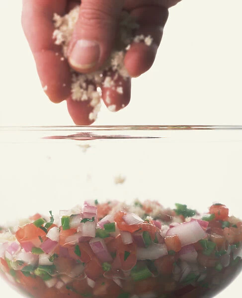 Close-up of sprinkling breadcrumbs over a salsa mixture in a glass bowl