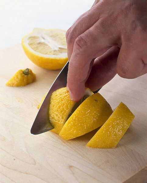 Using kitchen knife to slice raw lemon on wooden chopping board, close-up