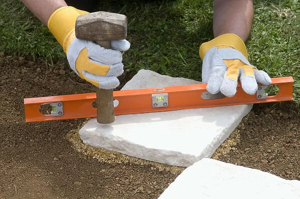 Using mallet and spirit level to position a paving slab, close-up