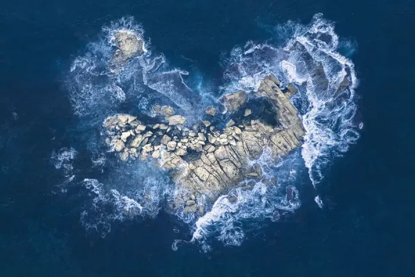 Ocean waves crashing over heart-shaped rock island