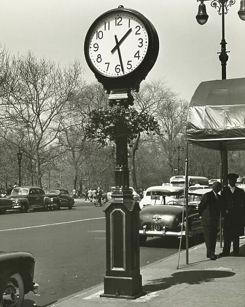 Decorative street clock, two background people standing on street, (B&W)