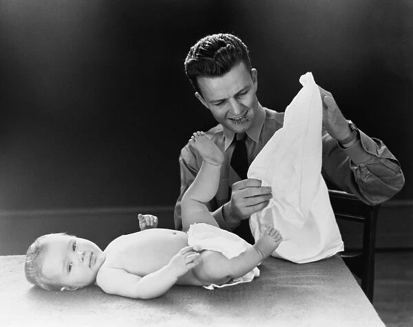 Young father with baby lying on table, trying to figure out how to put on diaper. (Photo by H