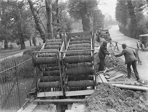 Bundles of telephone cables on a cradle that are being laid underground by workers