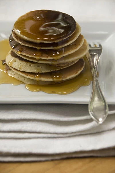 Stack of Scotch pancakes on white plate with silver fork and maple syrup credit