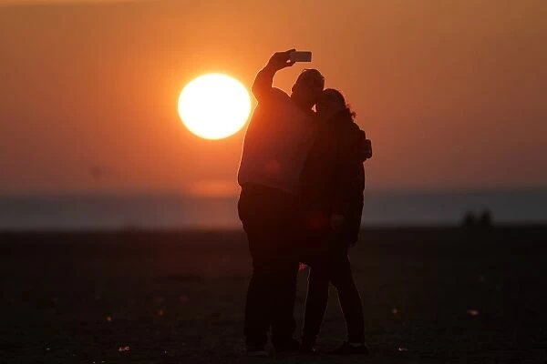 France-Theme-Love. A couple take a selfie photograph at sunset in Deauville