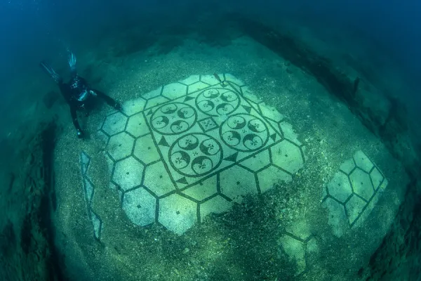 Scuba diver exploring splendid ancient Roman tessellatum mosaic in black and white decorated with pattern of hexagons, perfectly preserved, in Villa a Protiro. Marine Protected Area of Baia, Naples, Italy. Tyrrhenian sea. S