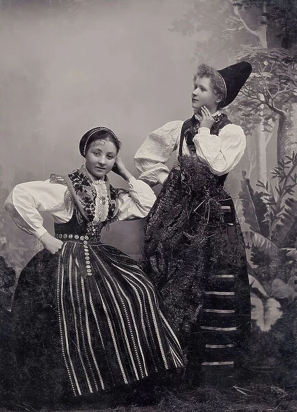 Studio portrait of two young girls posing in folk costumes from Dalarna, 1880-1907. Creator: Helene Edlund
