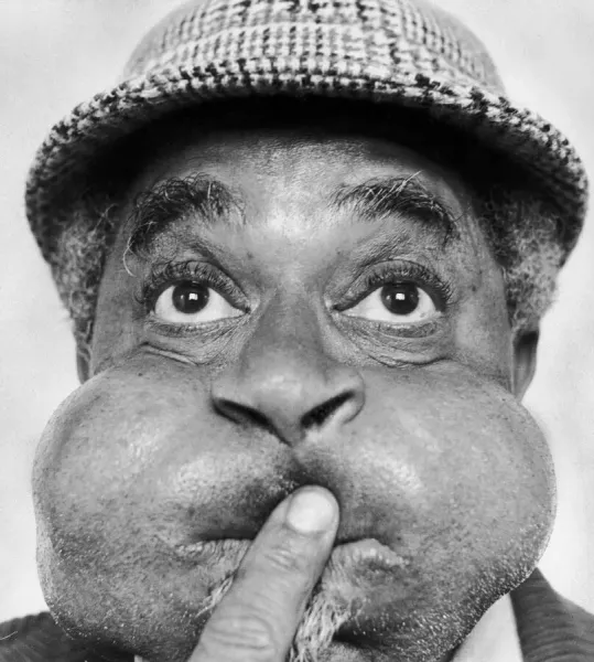 American jazz musician Dizzy Gillespie puffing out his cheeks during a visit to