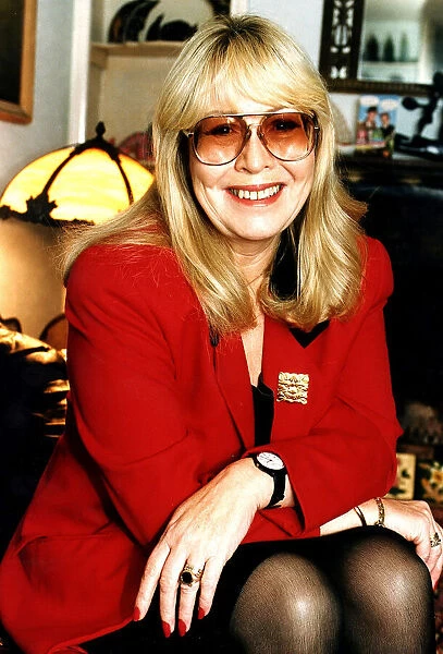 Cynthia Lennon wearing red jacket with arms on knees and dark glasses December 1995