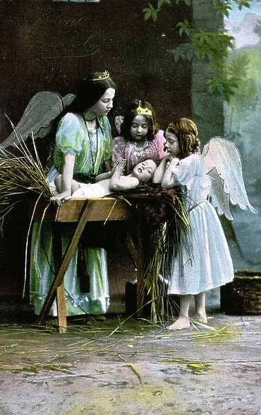 Christmas card with the Nativity. Three small girls dressed as angels are posing in an adoring position around a rudimentary cradle where the baby Jesus is lying