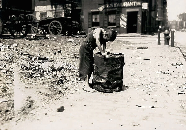 Deserted street of New York with a young barefooted boy dressed in rags rummaging in a trash can
