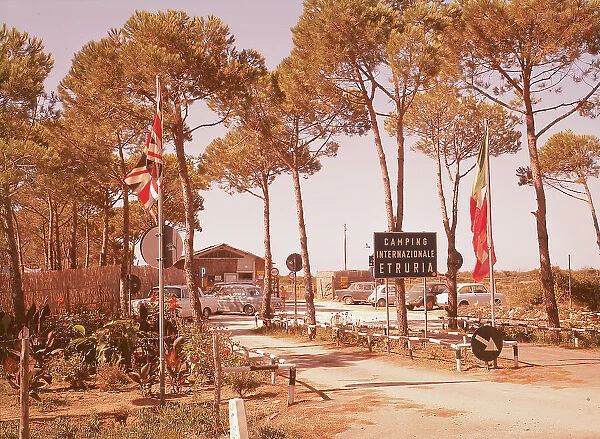Entrance to the Camping Internazionale Etruria, in a pine grove in Castiglione della Pescaia. A few cars are parked in front of the entrance. In the foreground two flagspoles with the english and italian flags