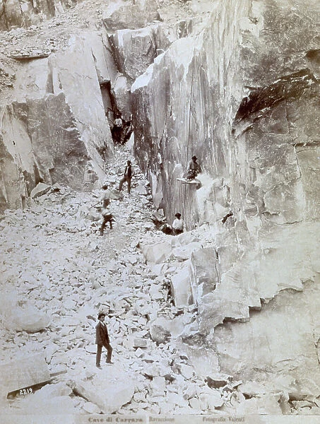 Group of quarriers at work in one of the quarries of Ravaccione (Carrara). A ravine with marble walls on each side has a floor strewen with blocks and fragments of various sizes